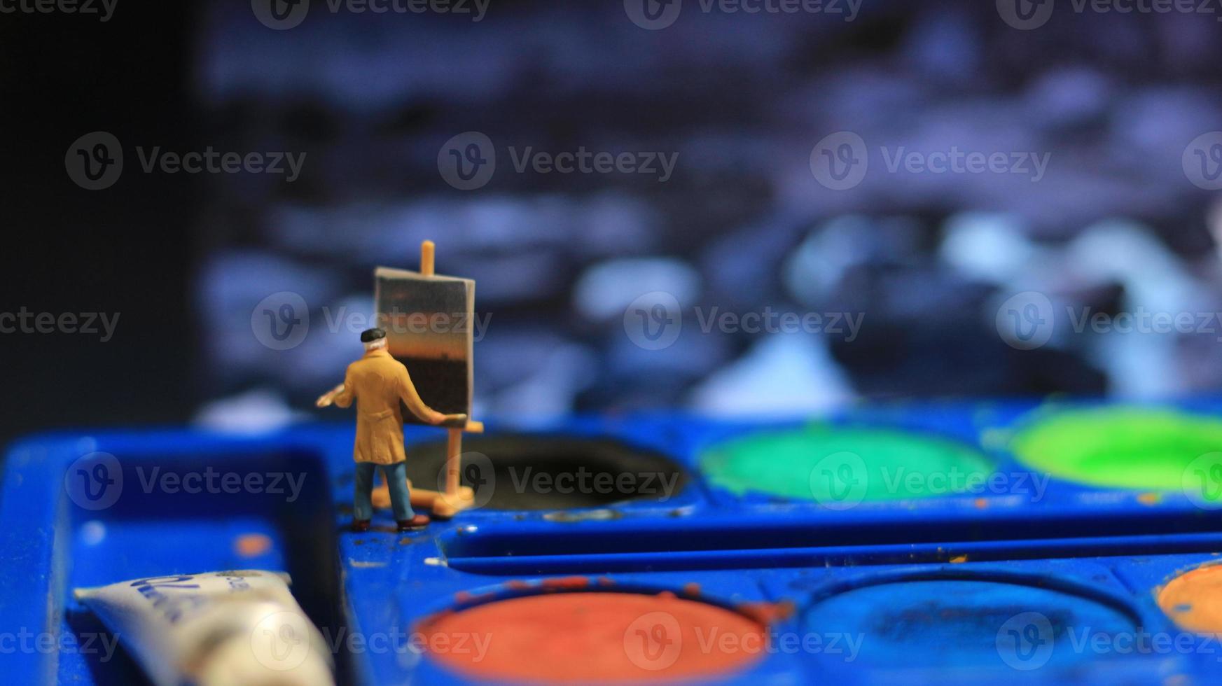 a miniature figure of a painter painting a landscape on watercolors. artist concept. photo