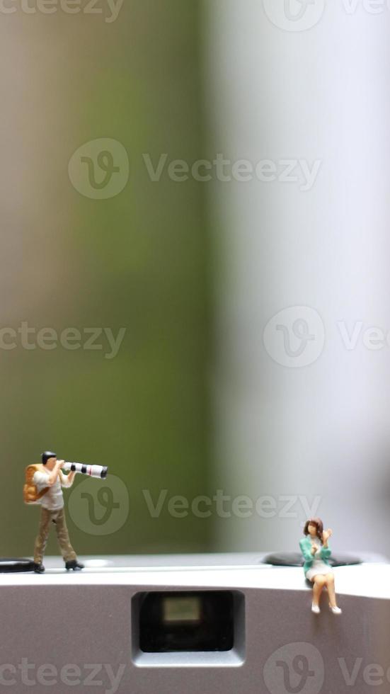 a miniature figure taking picture with a camera against a real camera in the background. photo