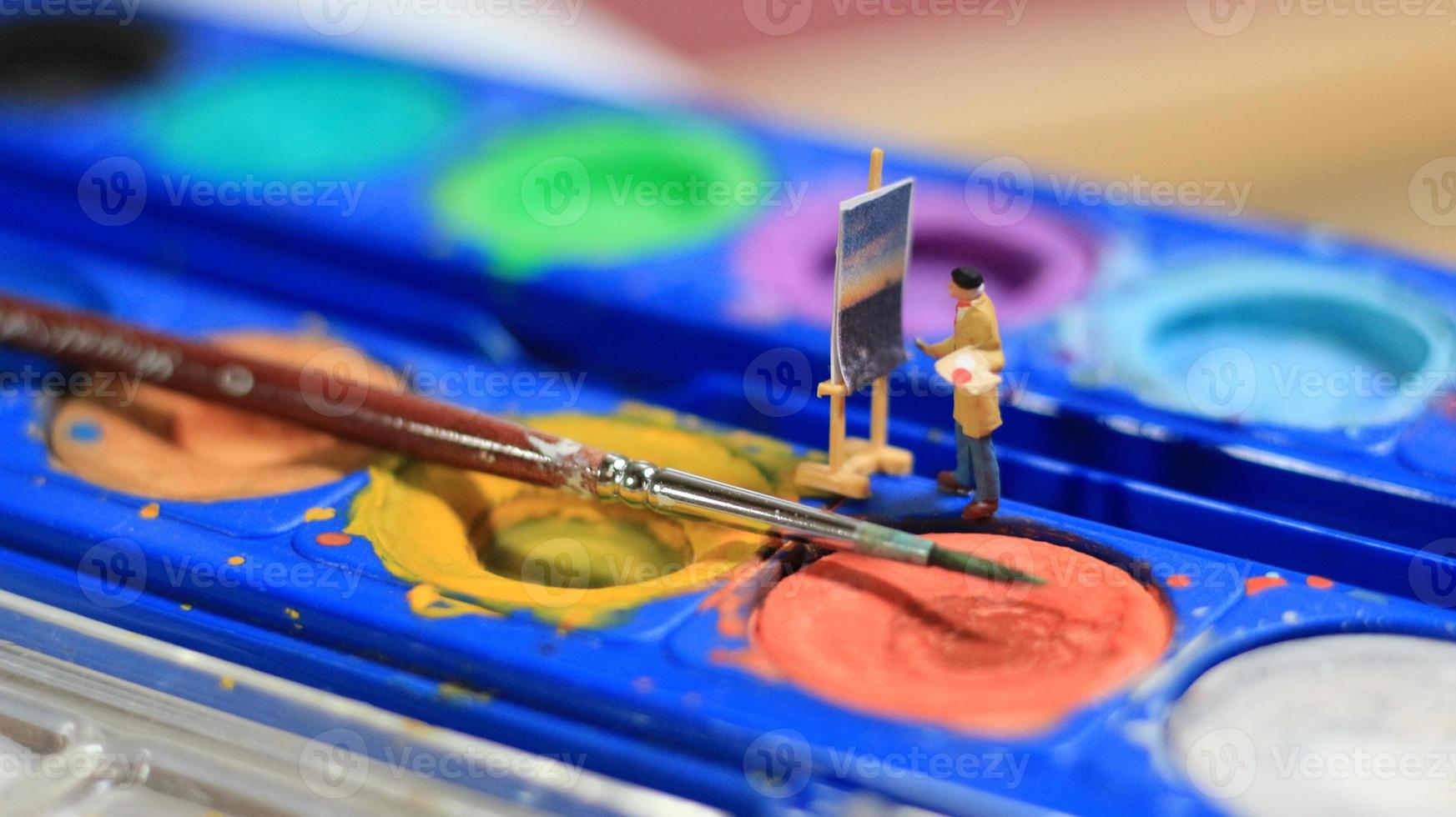 a miniature figure of a painter painting a landscape on watercolors. artist concept. photo