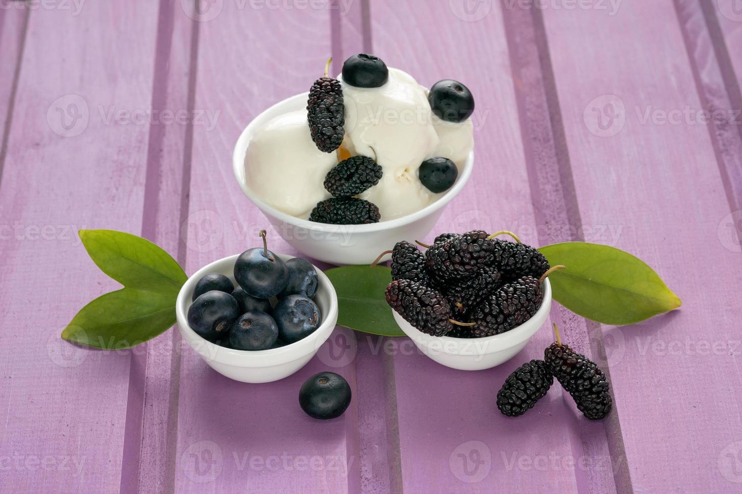 on a purple wooden background - plates with fresh blueberries and mulberries and a plate with ice cream balls with berries photo