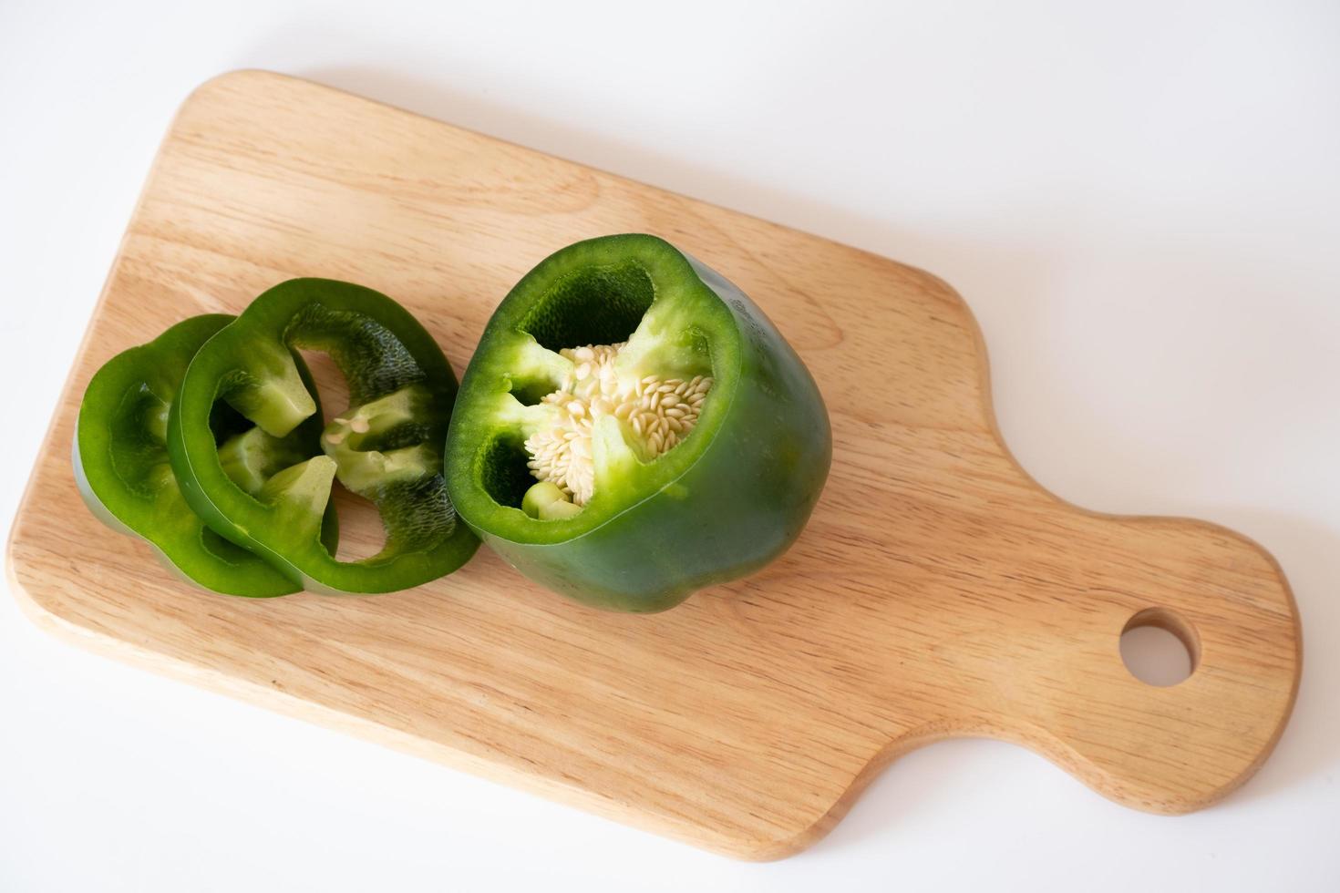 Cutting green sweet bell pepper on the wooden board isolated on white background. photo