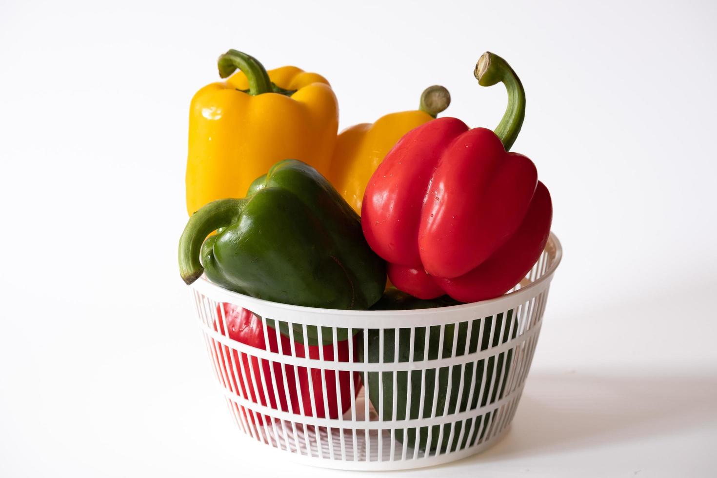 Sweet bell peppers in the white basket with water drops isolated on white background. photo
