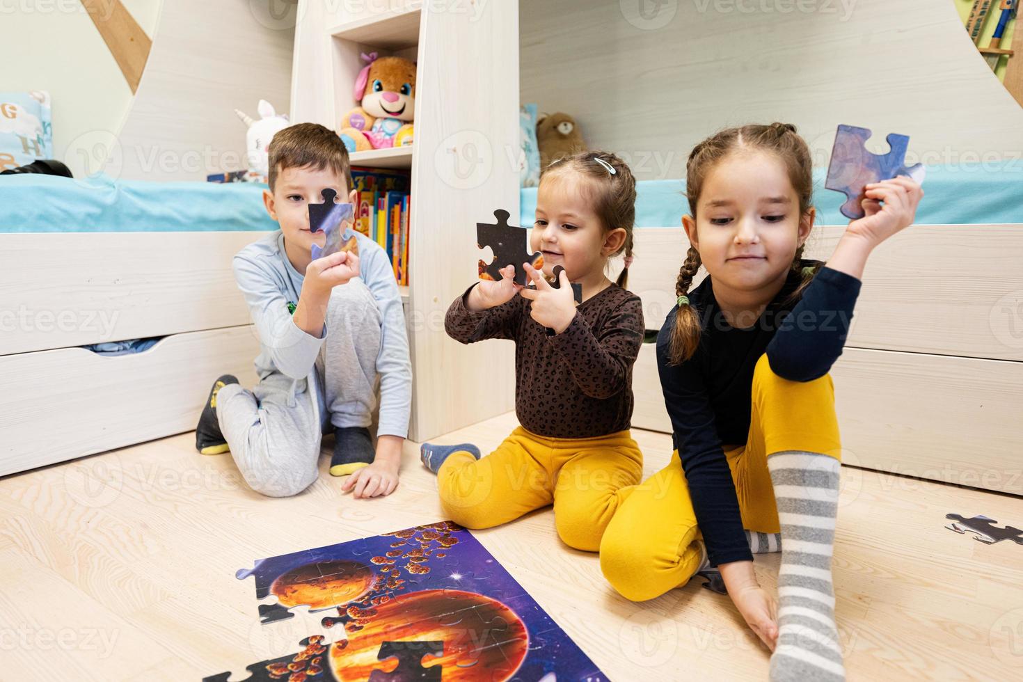 Children connecting jigsaw puzzle pieces in a kids room on floor at home.  Fun family activity leisure. photo