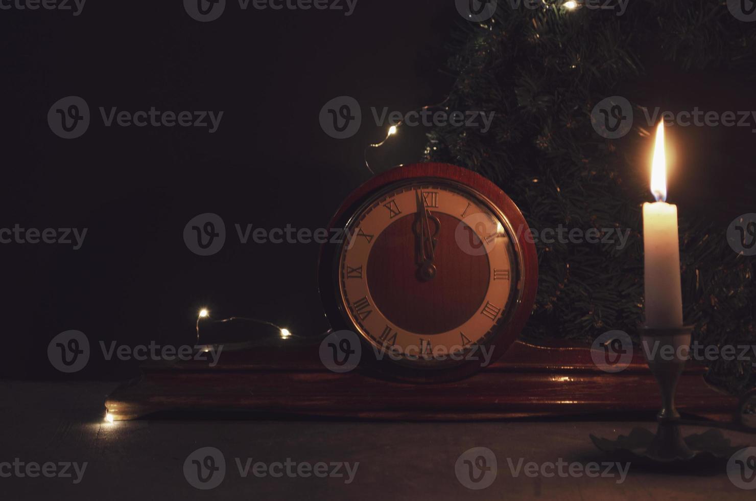 Vintage old wooden clock, yellow candle and Christmas tree branch on background. Midnight on clock. Burning candle. photo