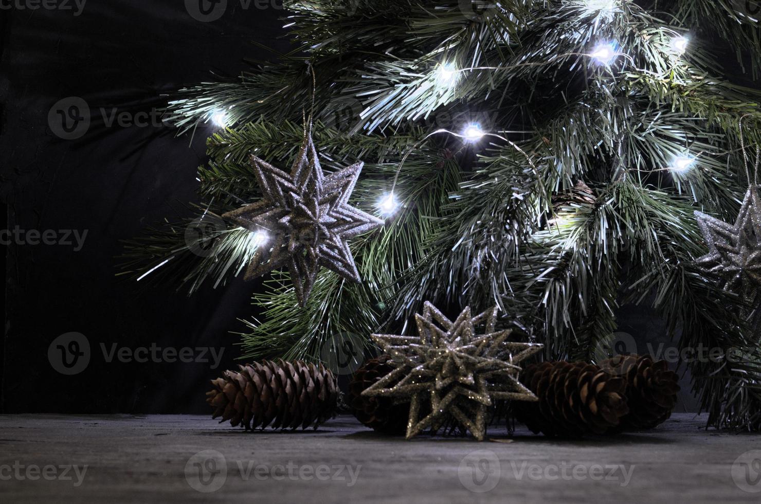 Silver snowflakes, pines and lighting garland on the spruce branch. Christmas still life in vintage style. Gray, black and silver colors. photo