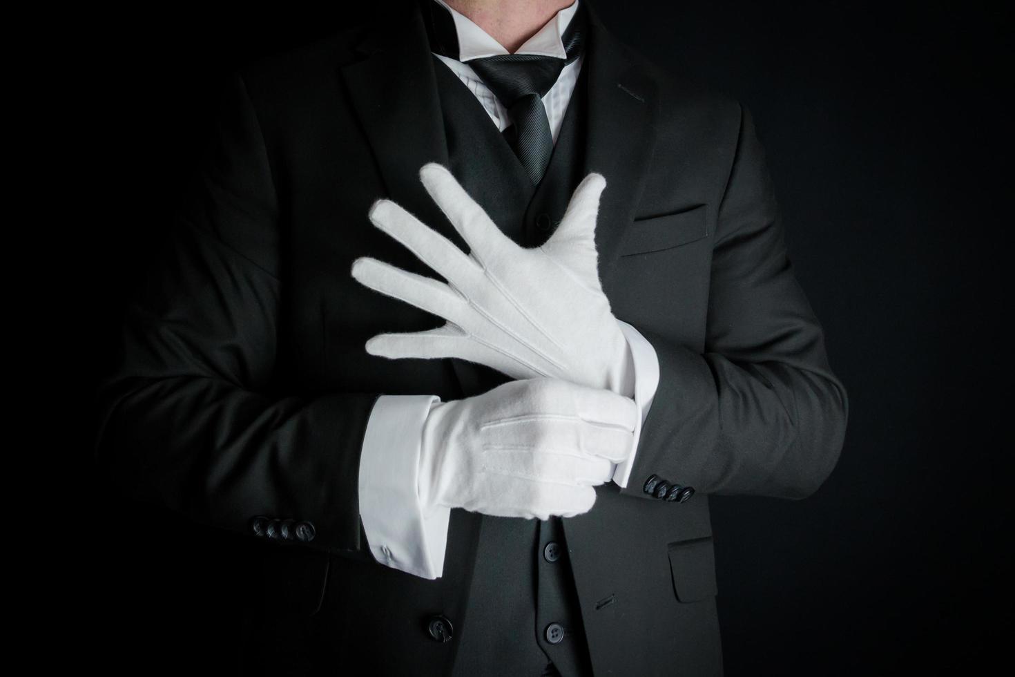 Portrait of Butler in Dark Suit on Black Background Pulling on Clean White Gloves. Concept of Service Industry and Professional Hospitality. photo