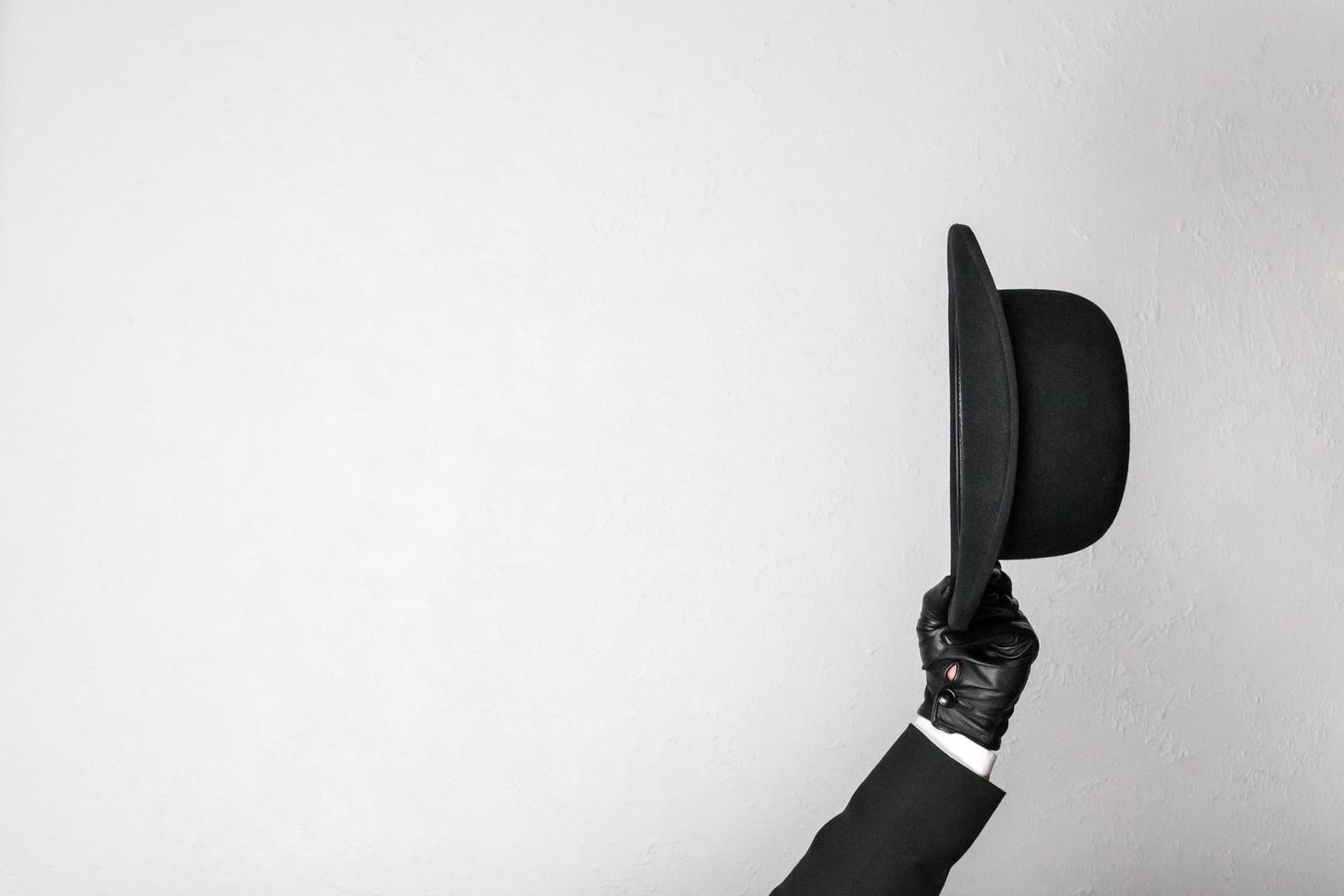 Isolated Image of Gentleman in Dark Suit and Leather Gloves Politely Doffing Bowler Hat. Classic British Butler or British Businessman. photo