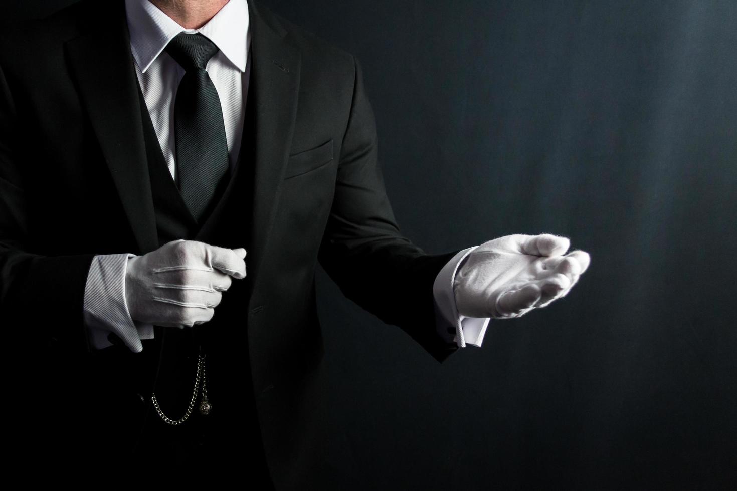 retrato de mayordomo en oscuro traje y blanco guantes ofrecimiento Ayudar mano. concepto de Servicio industria y profesional cortesía. foto