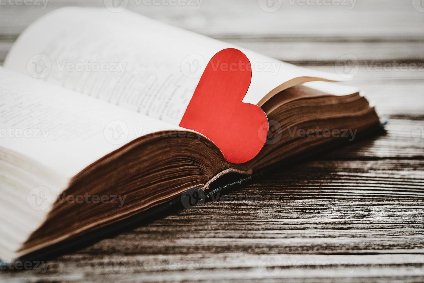 open book with red heart shaped paper bookmark on wooden background photo