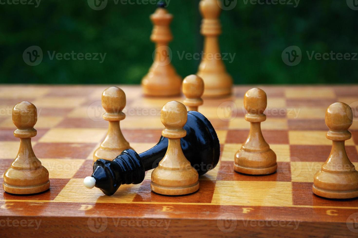 Checkmating - black chess queen fallen and surrounded by white pawns on the chessboard photo