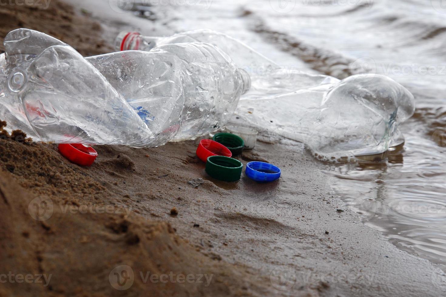 Plastic waste left by campers at river or lake shore, bottles and plastic bottle caps on the sand photo