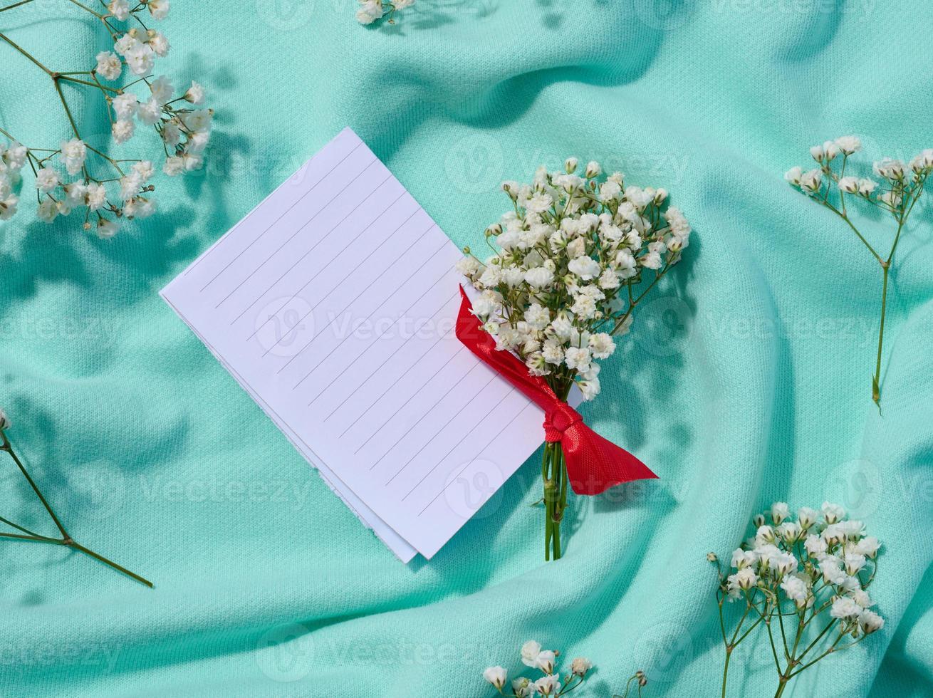 ramo de flores de del bebe aliento y doblada blanco papel en un textil fondo, un nota. parte superior ver foto