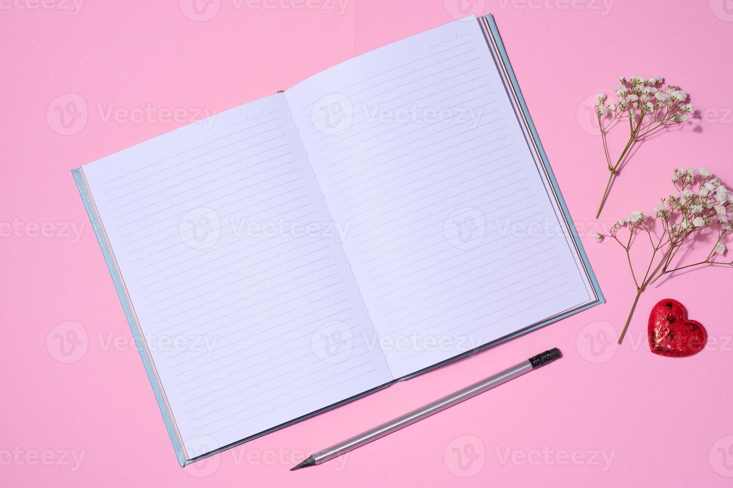 Open notebook, wooden pencil on pink background, top view photo