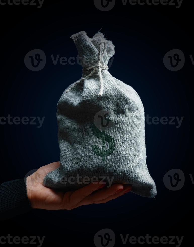 A female hand holding a full burlap sack with a dollar sign, concept of wealth, profitable business photo