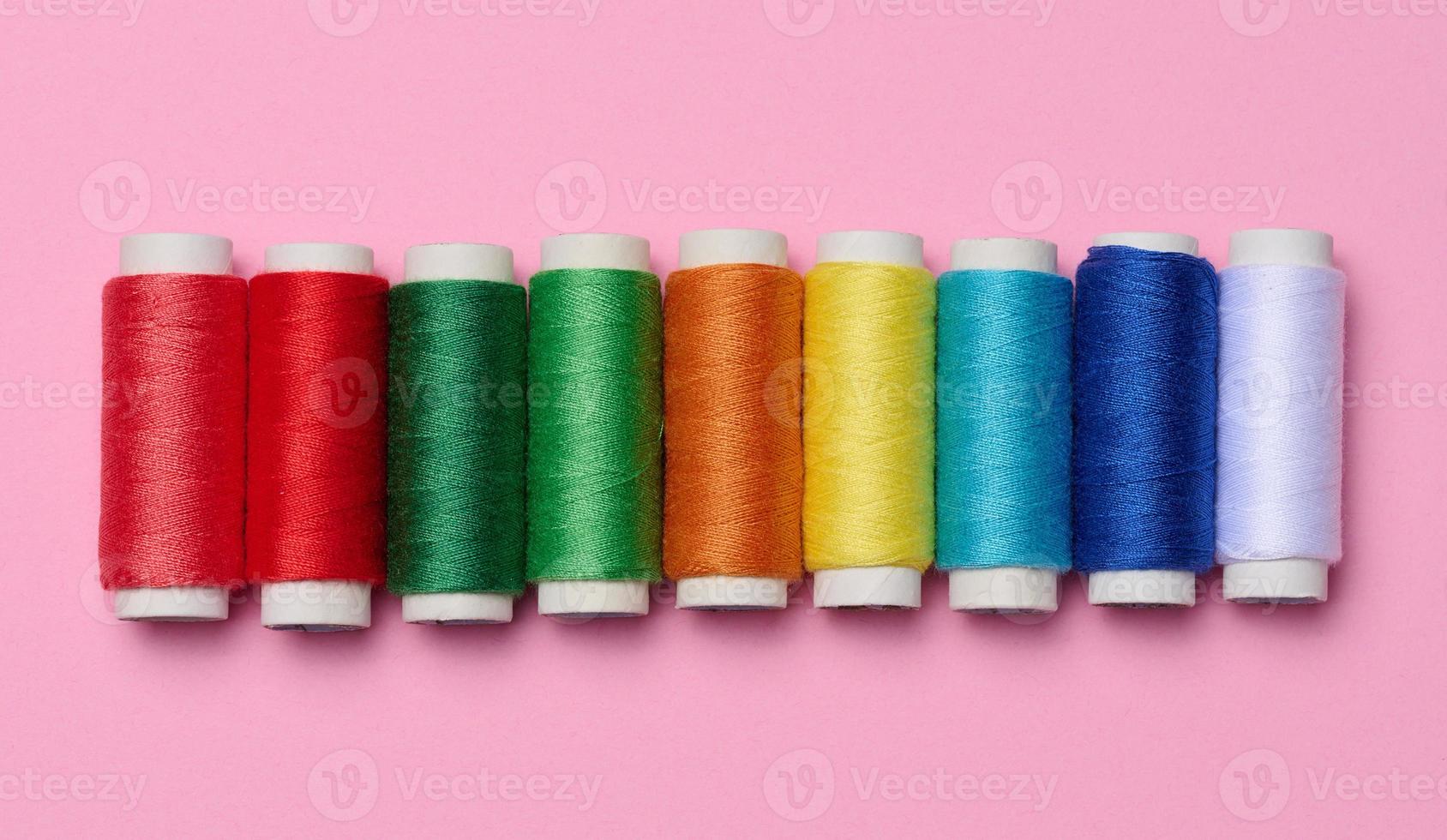 Multicolored spools of sewing threads on a pink background, top view photo