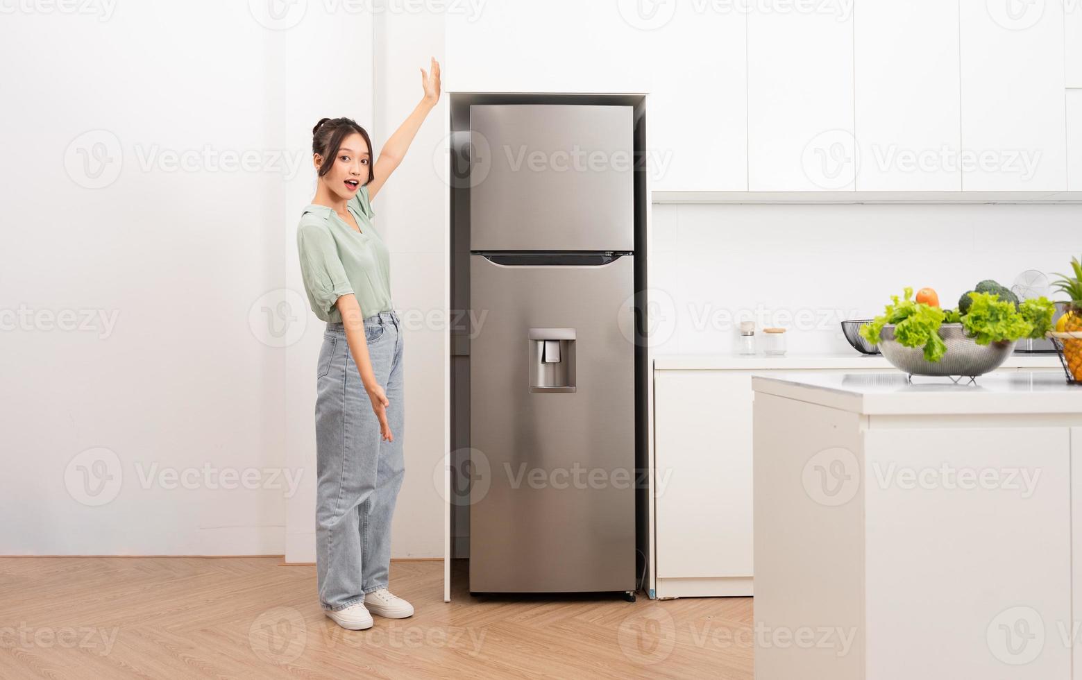 asiático mujer en pie siguiente a el refrigerador en el cocina foto