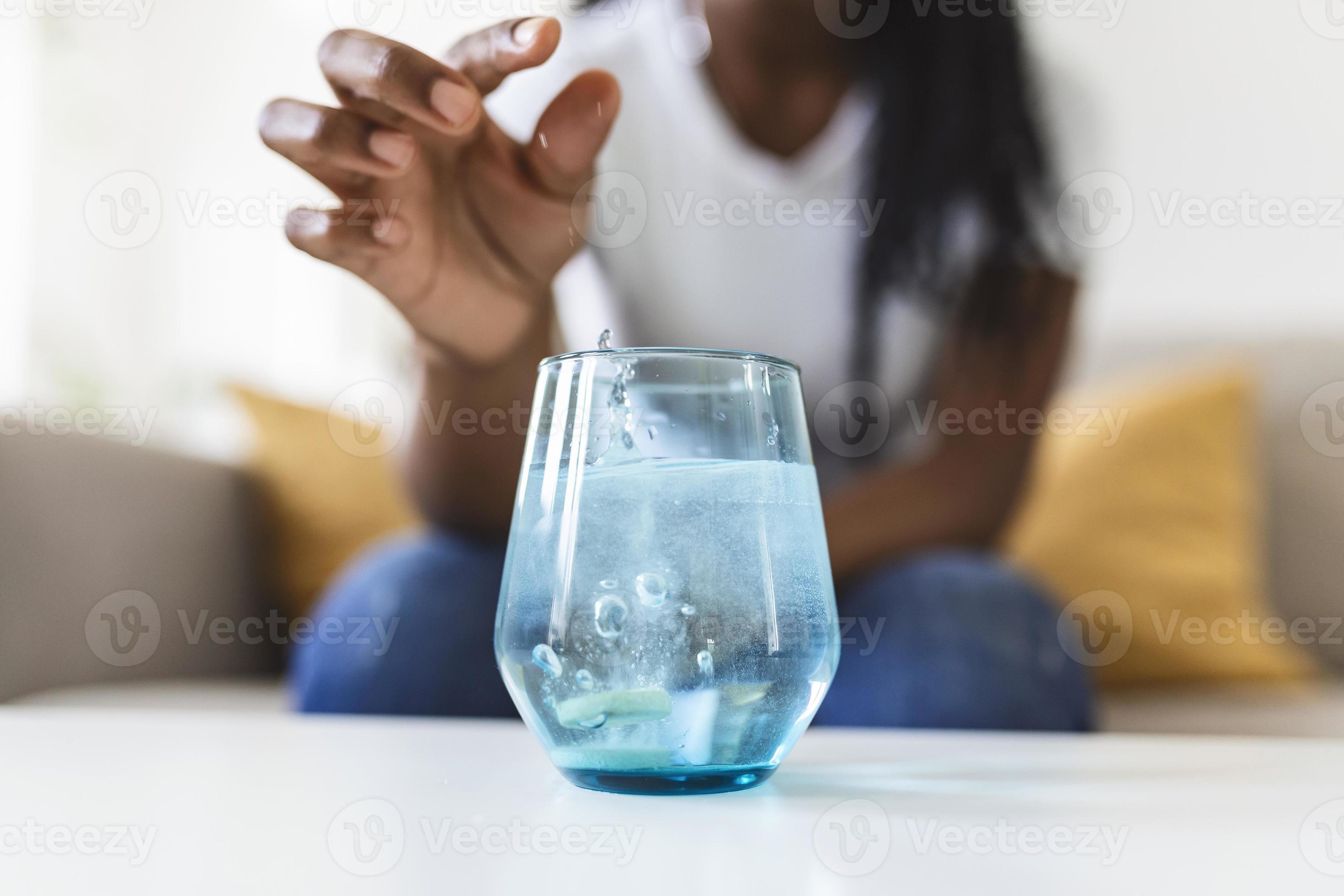 Closeup of a young woman dropping an effervescent antacid in a glass of