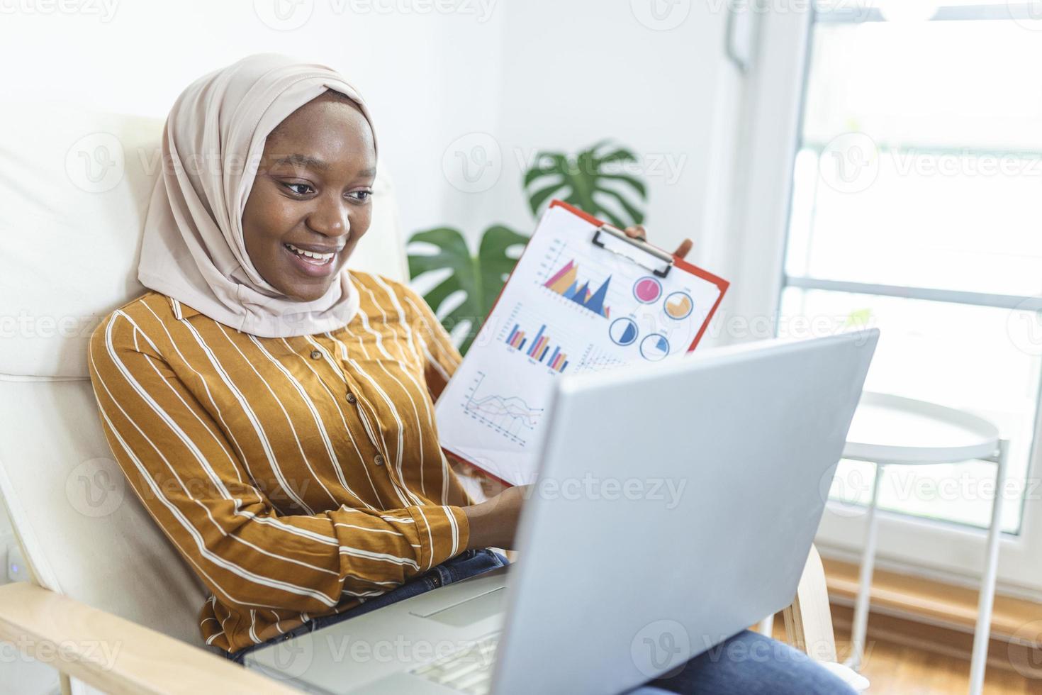 enfocado musulmán mujer de negocios presentación cartas y gráficos en vídeo llamada en línea. joven negocio mujer eh hijab teniendo conferencia llamada con cliente en ordenador portátil. trabajando ordenador portátil computadora interior. foto