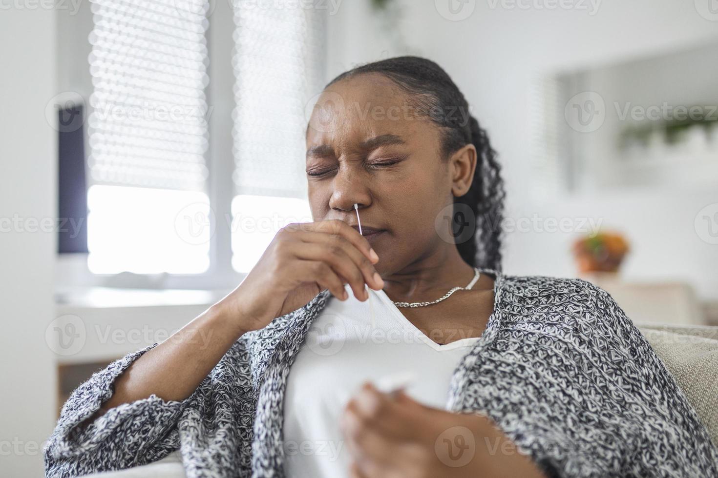 African-American woman using cotton swab while doing coronavirus PCR test at home. Woman using coronavirus rapid diagnostic test. Young woman at home using a nasal swab for COVID-19. photo