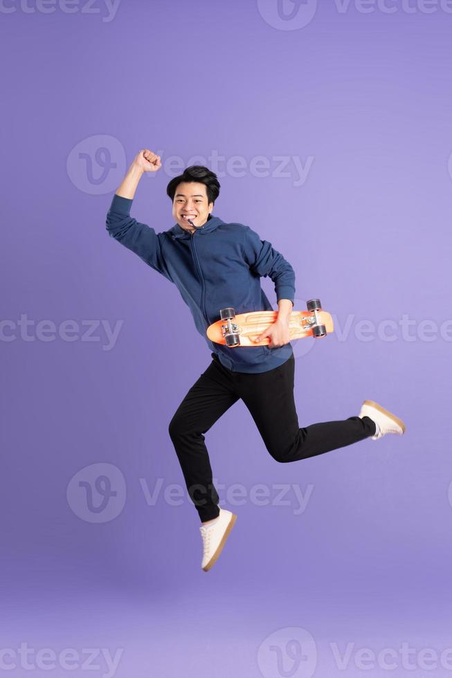 Image of young Asian man playing skateboard on purple background photo