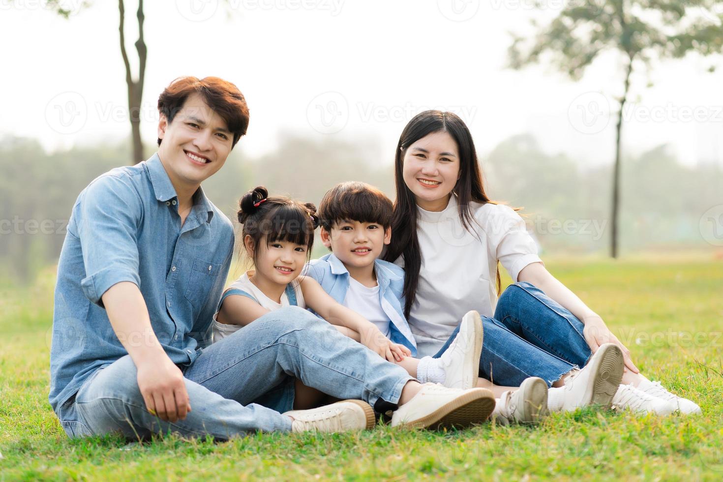 imagen de un asiático familia sentado juntos en el césped a el parque foto