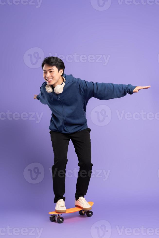 Image of young Asian man playing skateboard on purple background photo