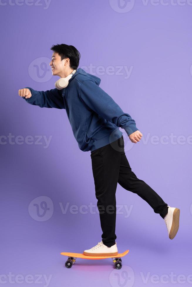 Image of young Asian man playing skateboard on purple background photo