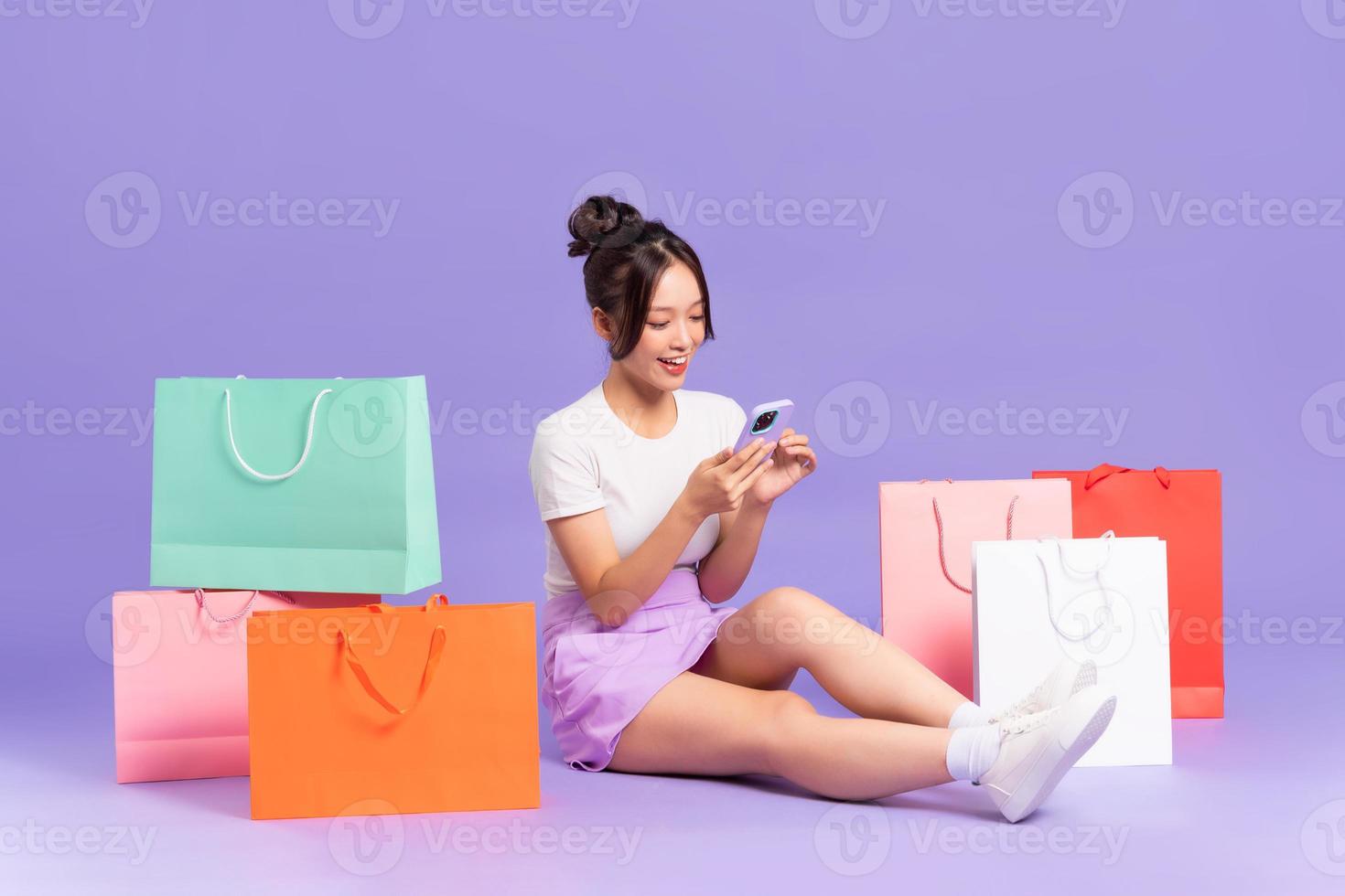 Young Asian woman holding shopping bag on purple background photo