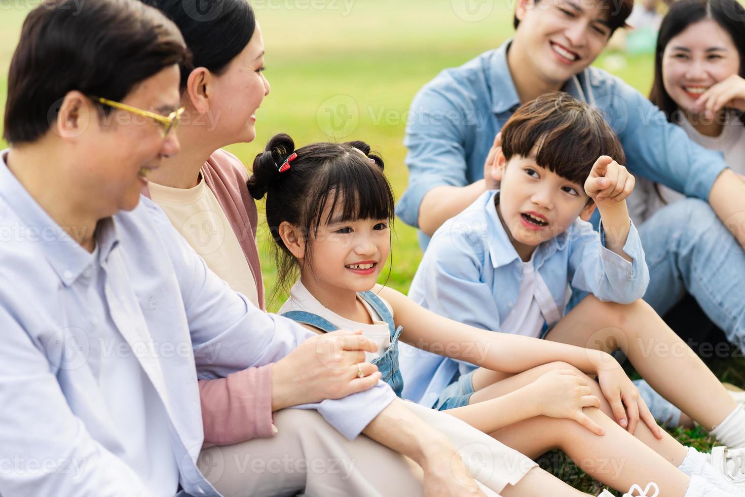 image of an asian family sitting together on the grass at the park photo