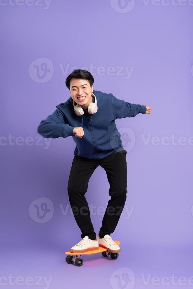 Image of young Asian man playing skateboard on purple background photo