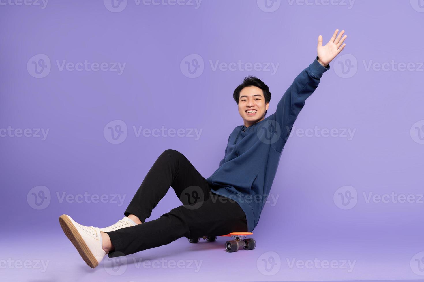 Image of young Asian man playing skateboard on purple background photo