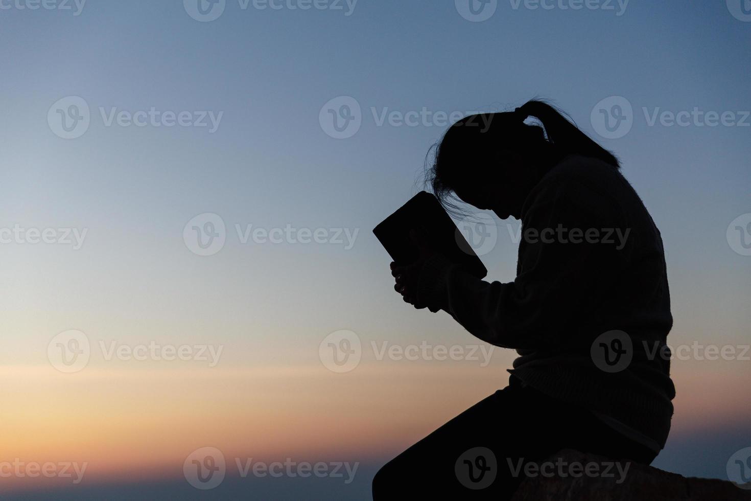 Silhouette of woman kneeling down praying for worship God at sky background. Christians pray to jesus christ for calmness. In morning people got to a quiet place and prayed. copy space. photo