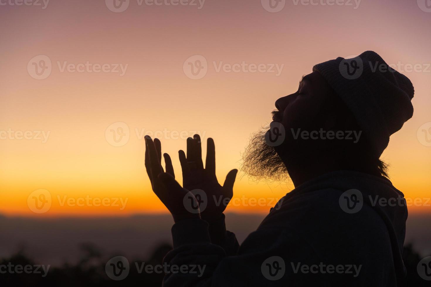 Silhouette of man kneeling down praying for worship God at sky background. Christians pray to jesus christ for calmness. In morning people got to a quiet place and prayed. copy space. photo