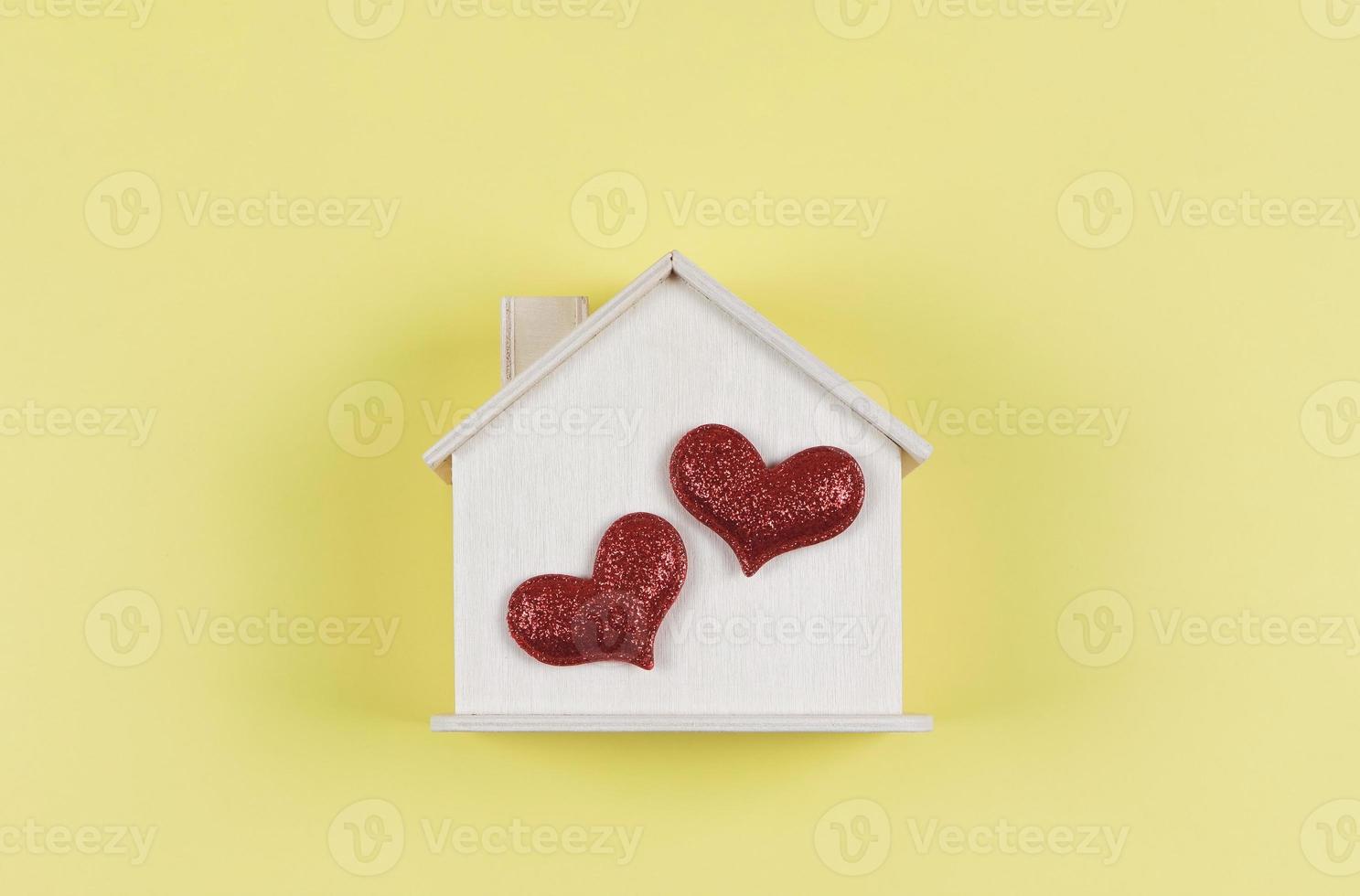 flat lay of wooden model house with two red glitter hearts on yellow  background. dream house , home of love, strong relationship, valentines. photo