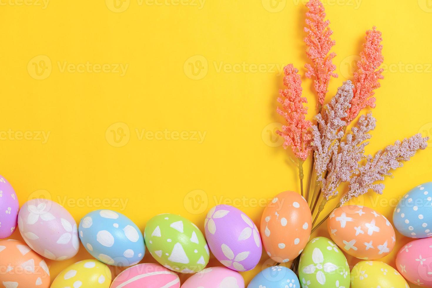 Happy Easter holiday greeting card design concept. Colorful Easter Eggs and spring flowers on yellow background. Flat lay, top view, copy space. photo
