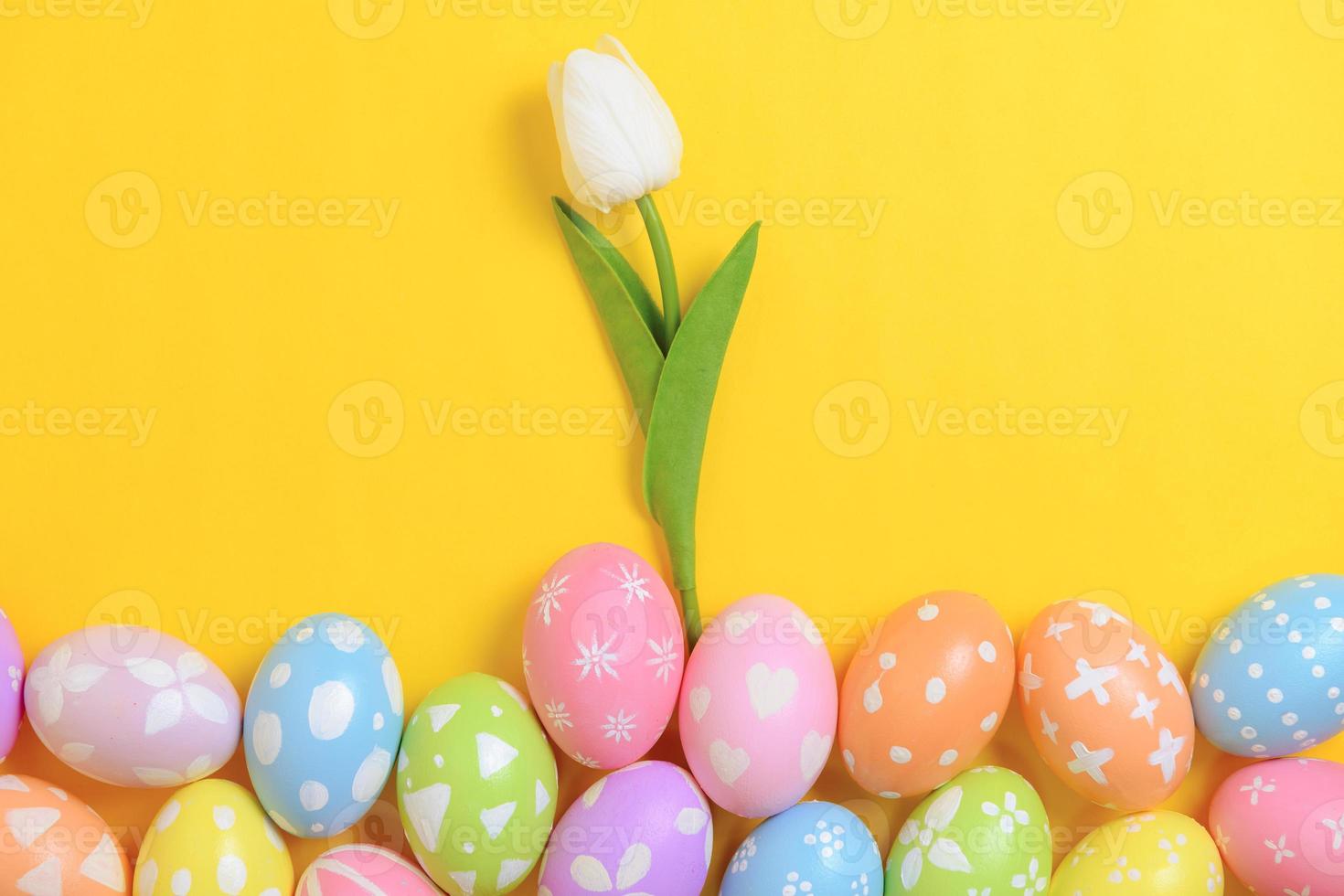 Happy Easter holiday greeting card design concept. Colorful Easter Eggs and spring flowers on yellow background. Flat lay, top view, copy space. photo