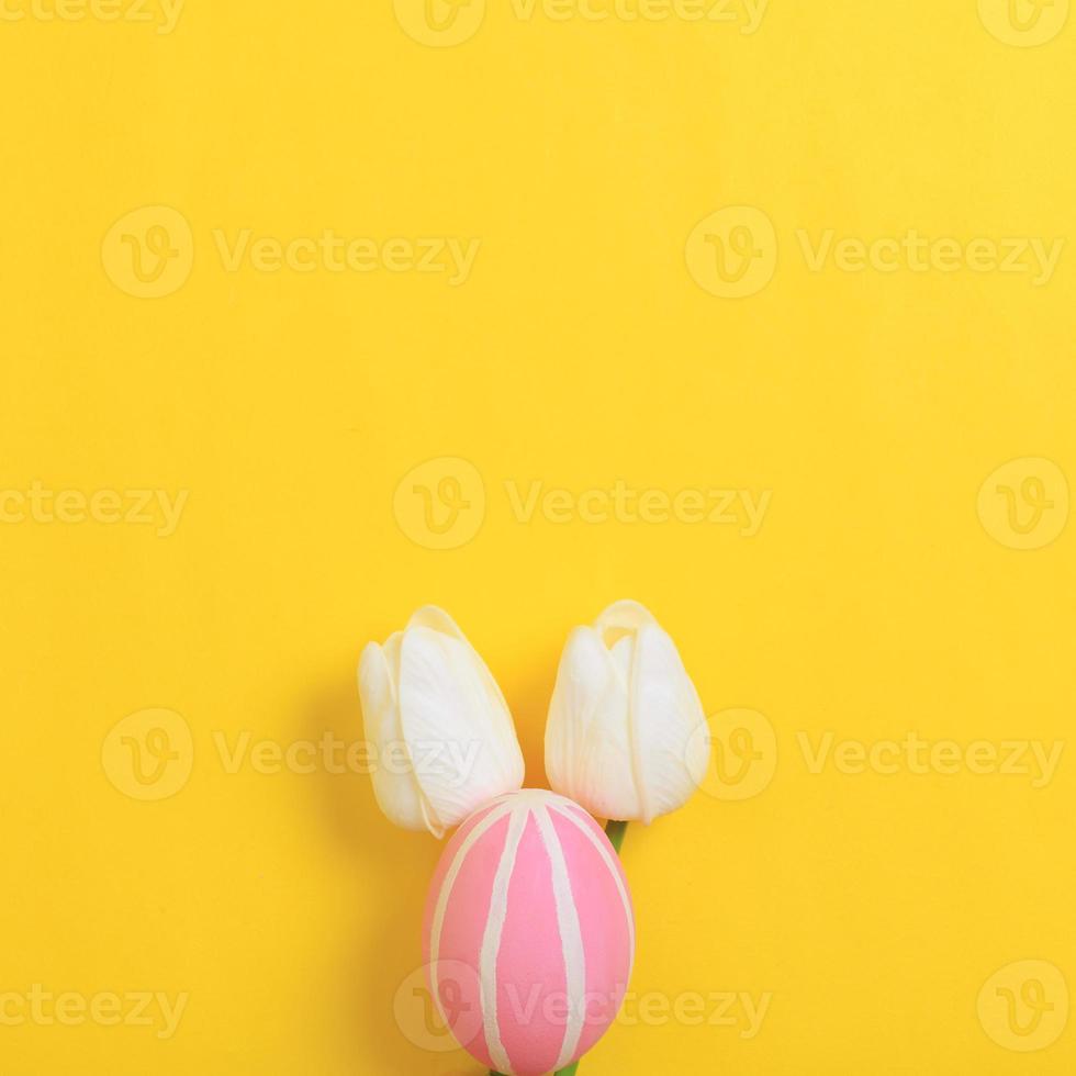 Happy Easter holiday greeting card design concept. Colorful Easter Eggs and spring flowers on yellow background. Flat lay, top view, copy space. photo