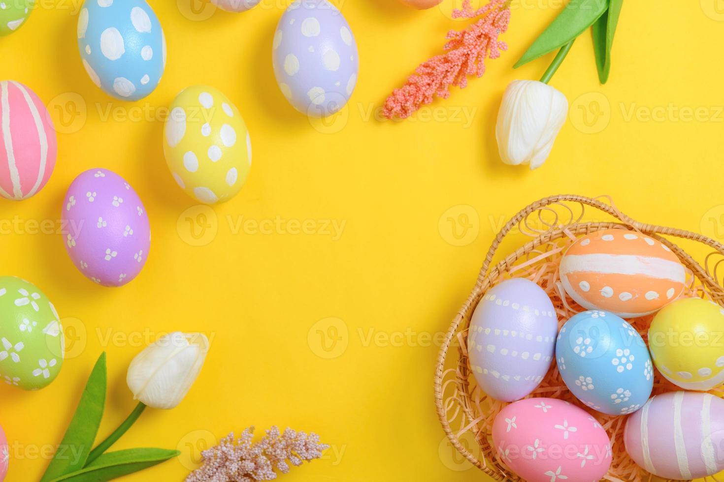 Happy Easter holiday greeting card design concept. Colorful Easter Eggs and spring flowers on yellow background. Flat lay, top view, copy space. photo