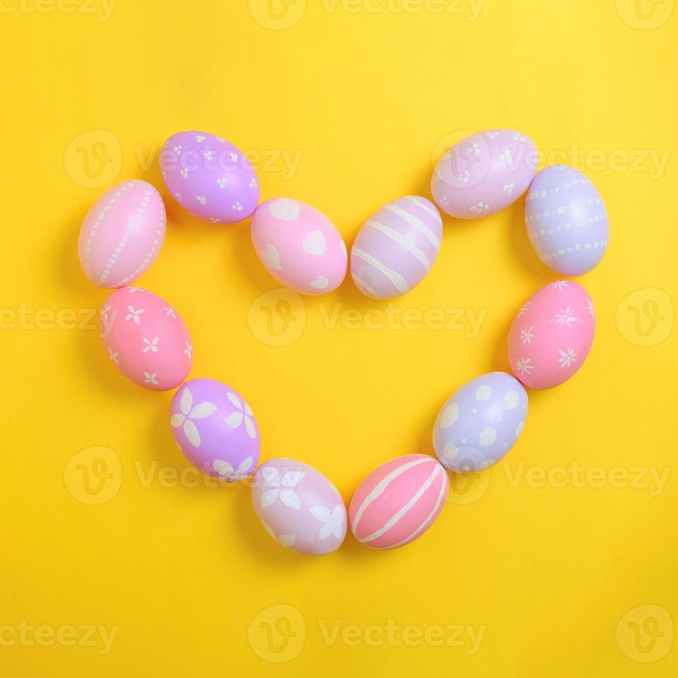 Happy easter holiday celebration concept. Group of painted colourful eggs in heart shape decoration on a yellow background. Seasonal religion tradition design. Top view, flat lay, copy space. photo