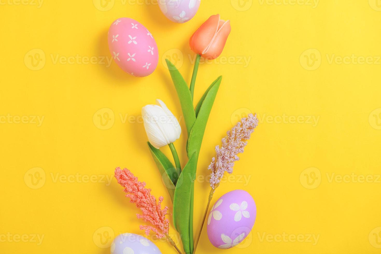 Happy Easter holiday greeting card design concept. Colorful Easter Eggs and spring flowers on yellow background. Flat lay, top view, copy space. photo