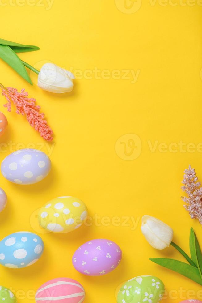 Happy Easter holiday greeting card design concept. Colorful Easter Eggs and spring flowers on yellow background. Flat lay, top view, copy space. photo