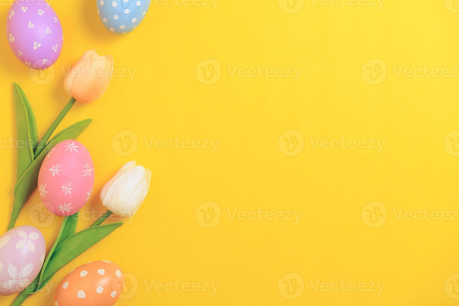 Happy Easter holiday greeting card design concept. Colorful Easter Eggs and spring flowers on yellow background. Flat lay, top view, copy space. photo