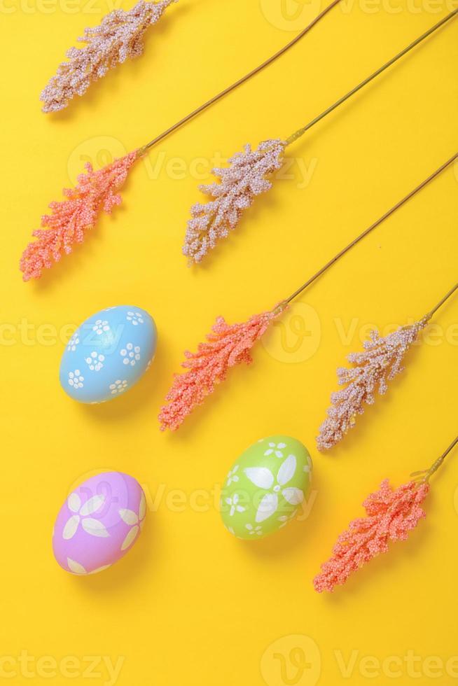 Happy Easter holiday greeting card design concept. Colorful Easter Eggs and spring flowers on yellow background. Flat lay, top view, copy space. photo