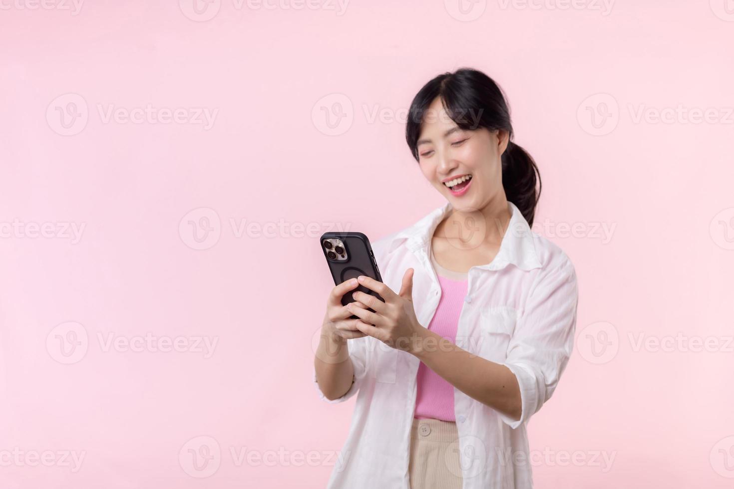 bonito joven asiático mujer demostración éxito, victoria mano gesto mientras recepción genial Noticias desde teléfono inteligente en rosado antecedentes. contento tecnología, móvil teléfono anuncio publicitario, en línea solicitud concepto foto
