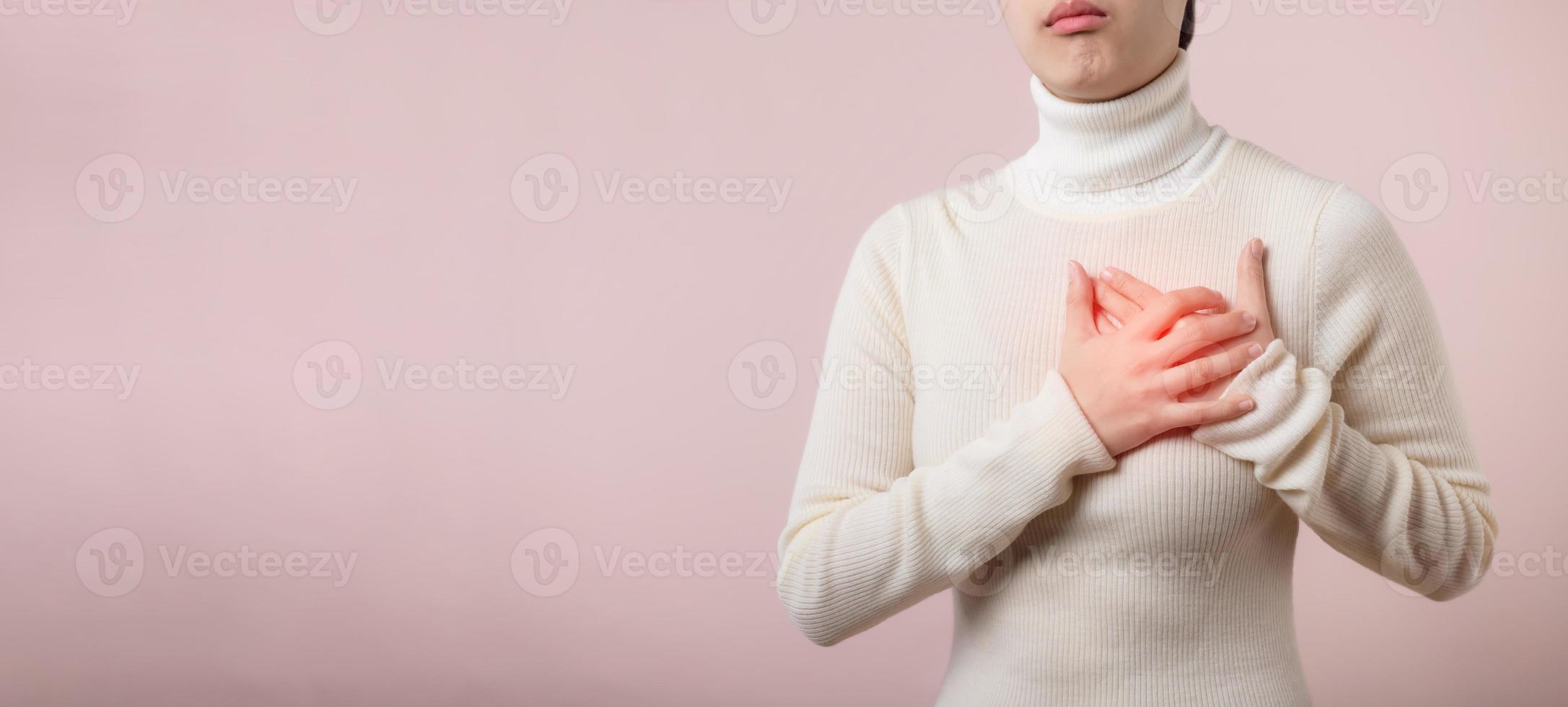 joven mujer sufrimiento desde corazón ataque en ligero rosado estudio antecedentes. doloroso calambre, corazón enfermedad, prensado en cofre con doloroso expresión. cuidado de la salud mundo salud día concepto. foto