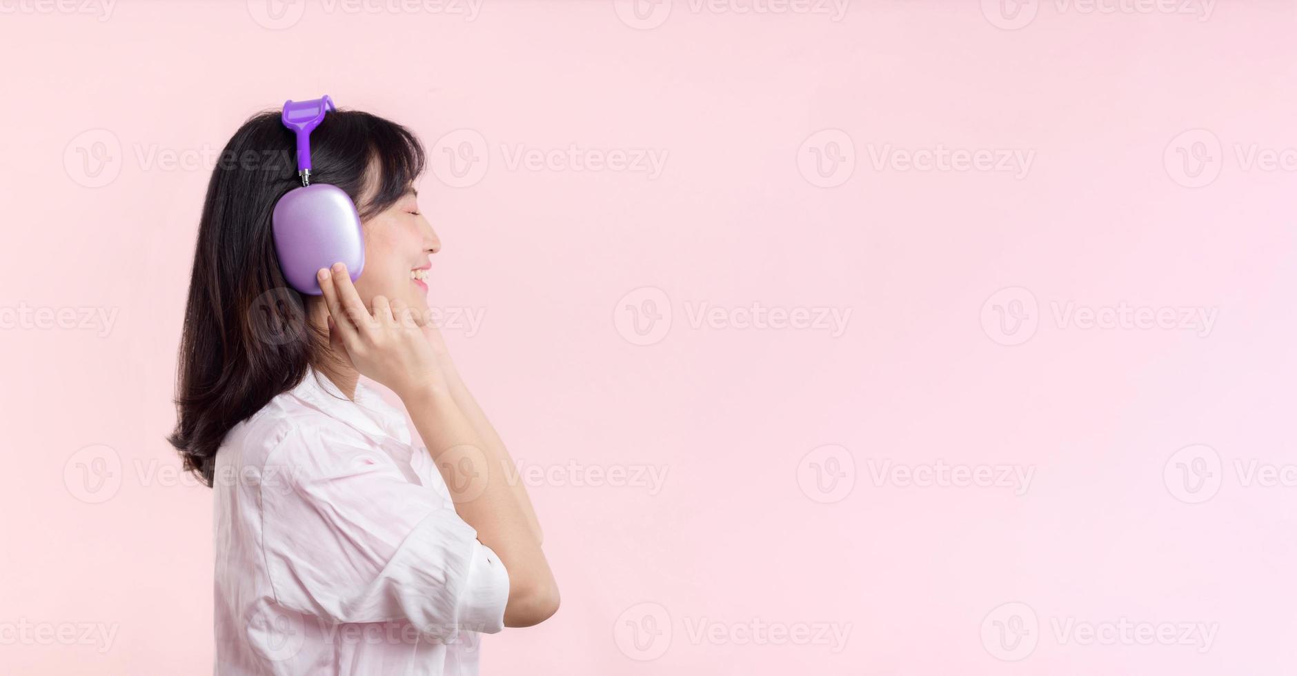 Side view young smiling cheerful fun woman she wear pink shirt white t-shirt headphones listen to music use mobile cell phone isolated on plain pastel light pink background. People lifestyle concept. photo