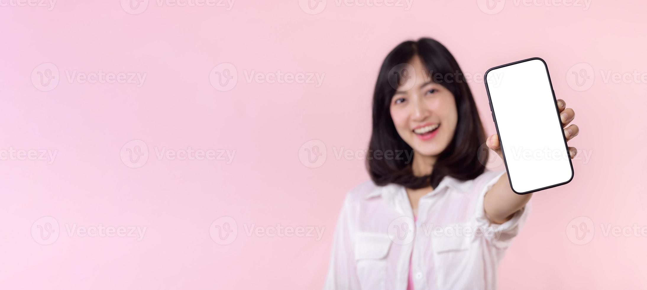 happy smiling young asian woman recommending showing new application or mobile advertisement, mockup smartphone template banner isolated on pink background. Collage blank screen digital mobile device. photo