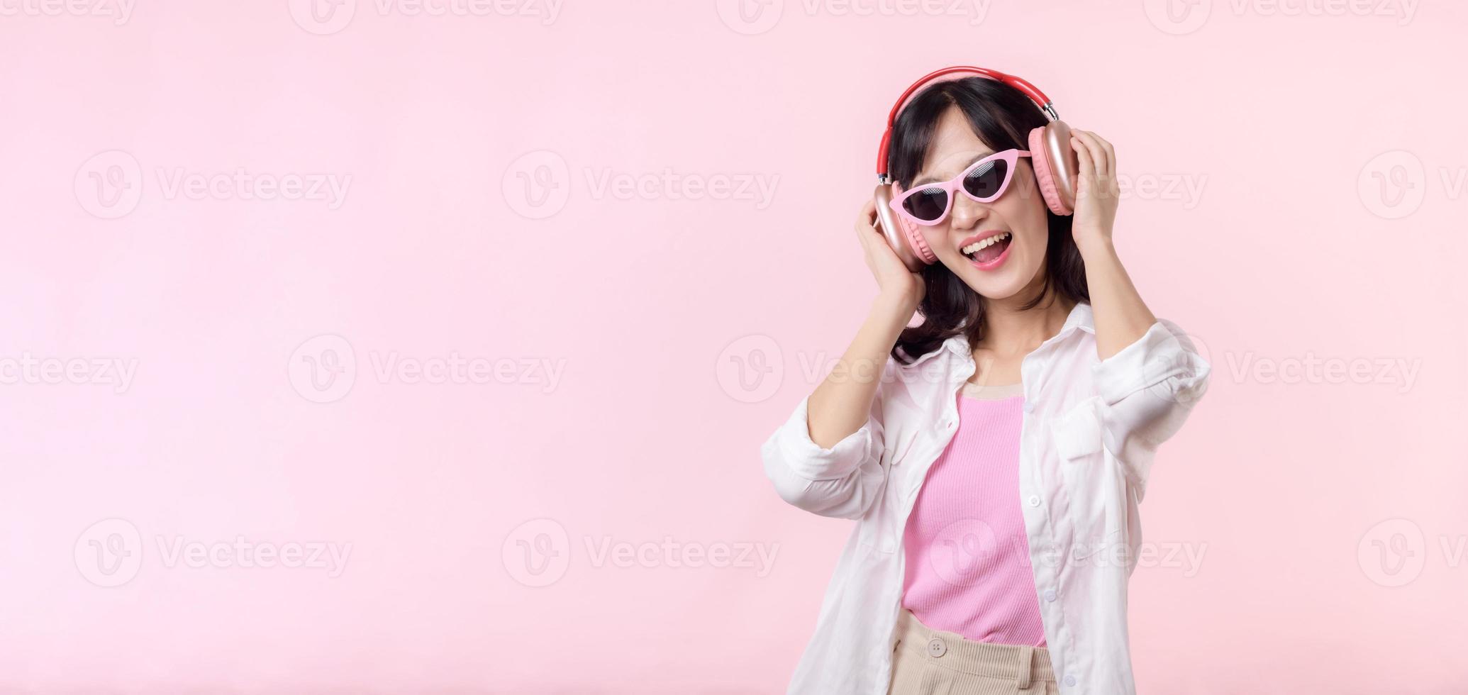 happy young asian woman model with stylish trendy sun glasses enjoy listening music by headphone audio and dancing isolated on pink studio background. technology, girl fashion, accessory concept. photo