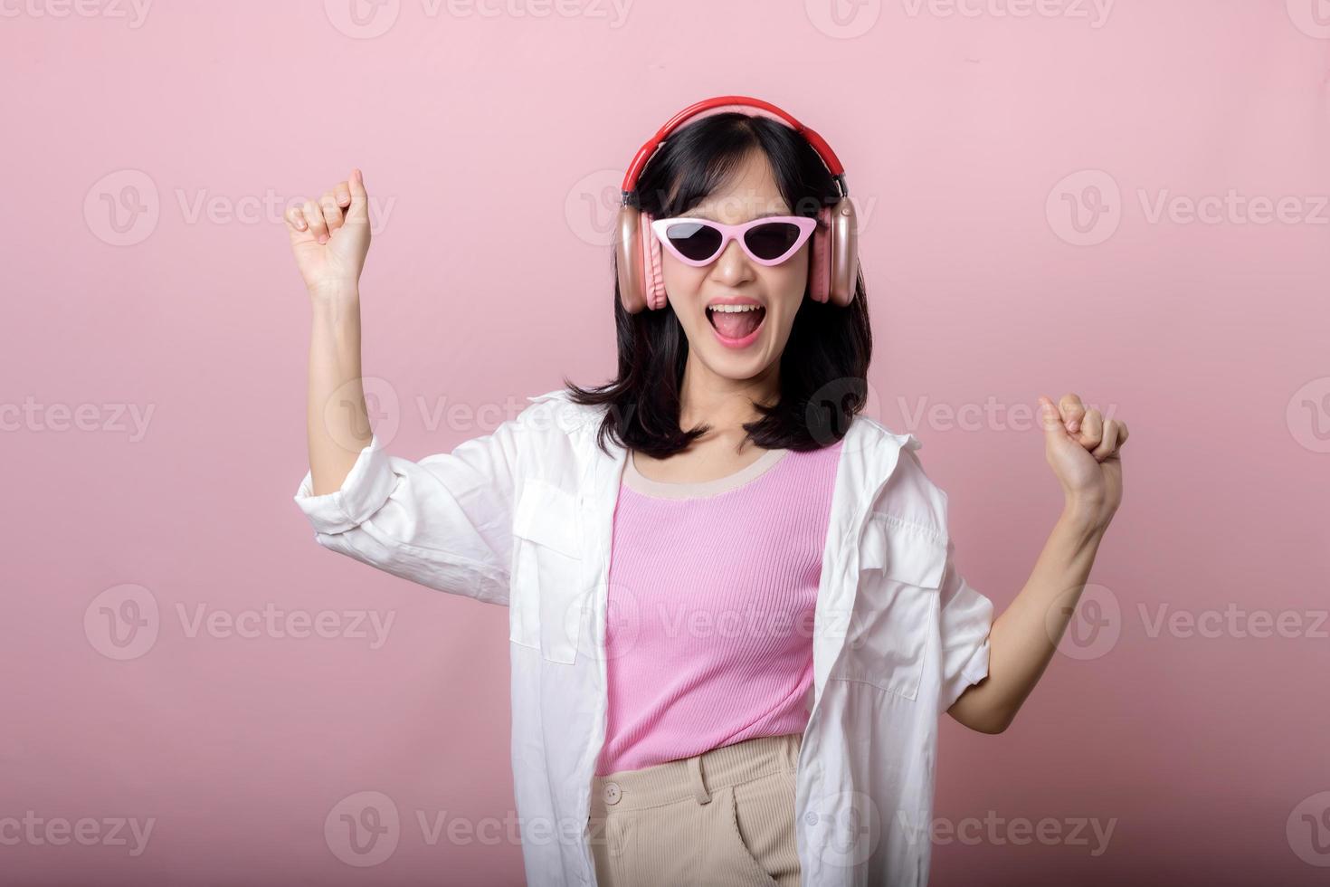 contento joven asiático mujer modelo con elegante de moda Dom lentes disfrutar escuchando música por auricular audio y bailando aislado en rosado estudio antecedentes. tecnología, niña moda, accesorio concepto. foto