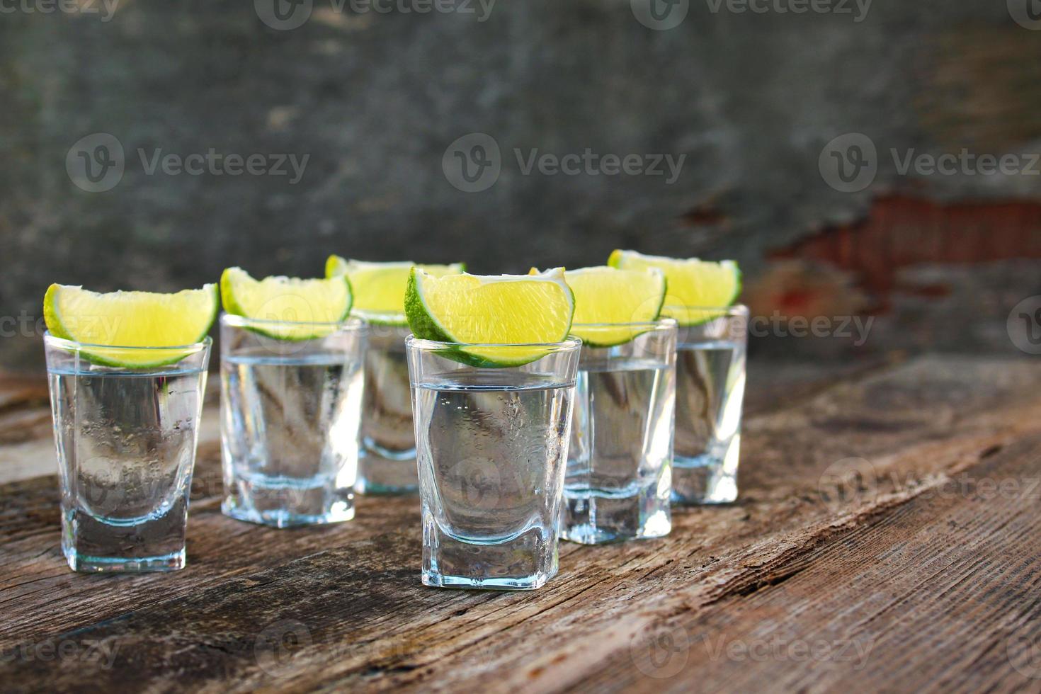 Vodka and lime slices on wooden background. photo